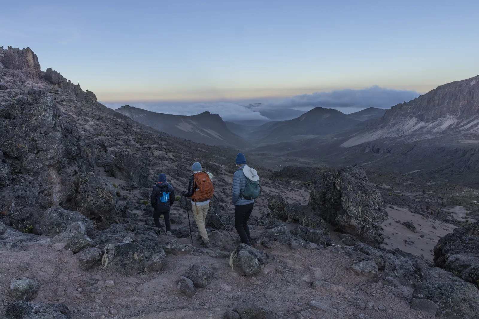 Three trekkers looking out over a rocky valley above the clouds on Mount Kenya
