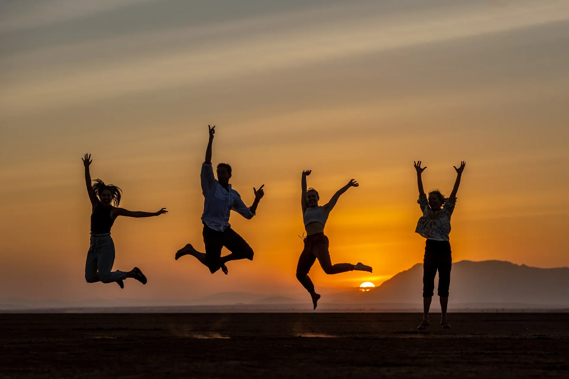Four travelers leaping in silhouette against a Kenyan sunset